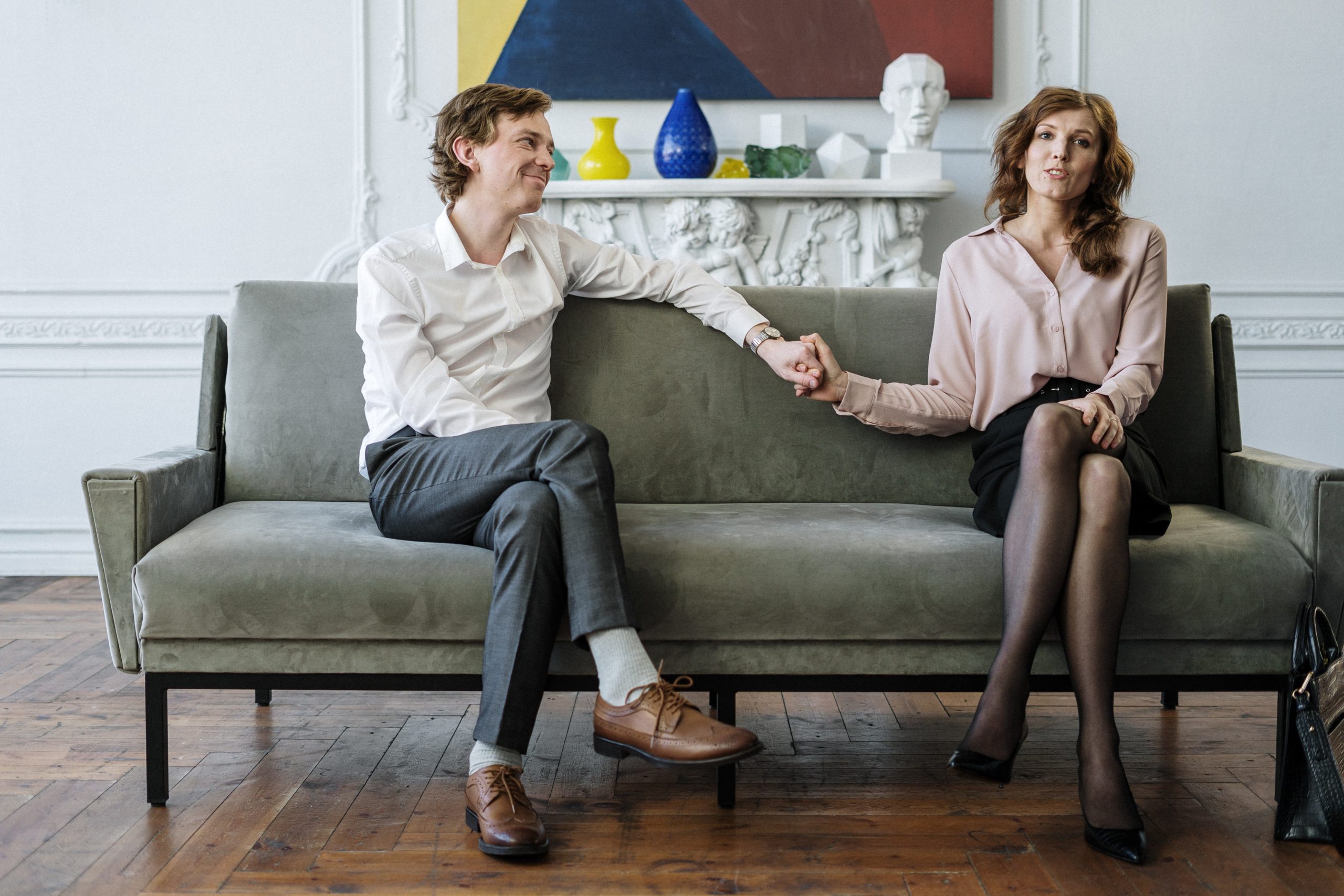 White mid-thirties couple holding hands on the couch